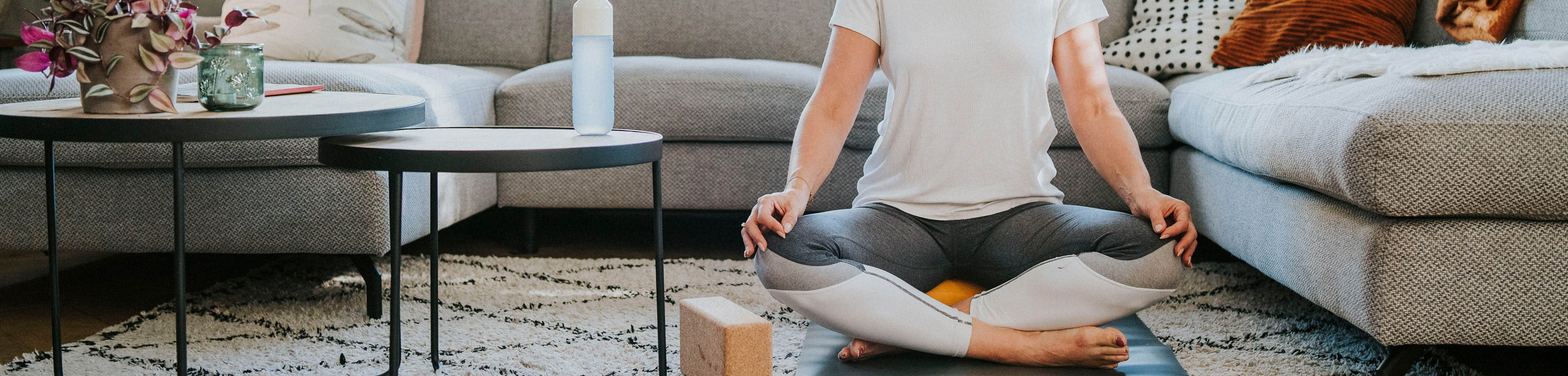 Vrouw zit in kleermakerszit op het kleed in de woonkamer.