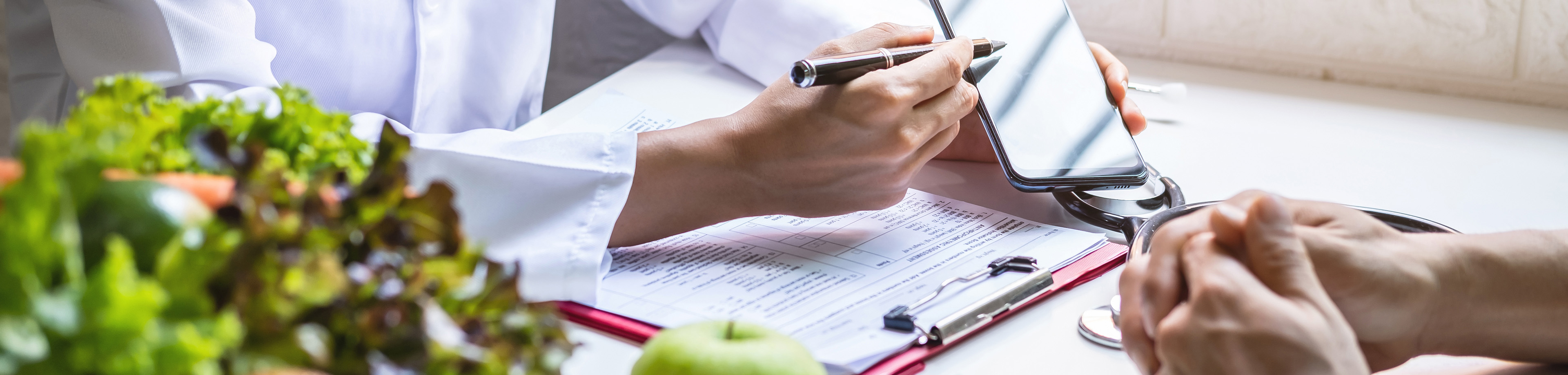Iemand in een witte doktersjas wijst met een pen iets aan op een telefoon. 