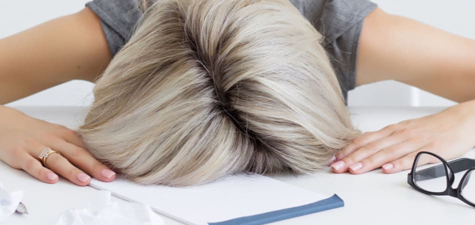 Vrouw met haar hoofd tussen haar handen op het bureau