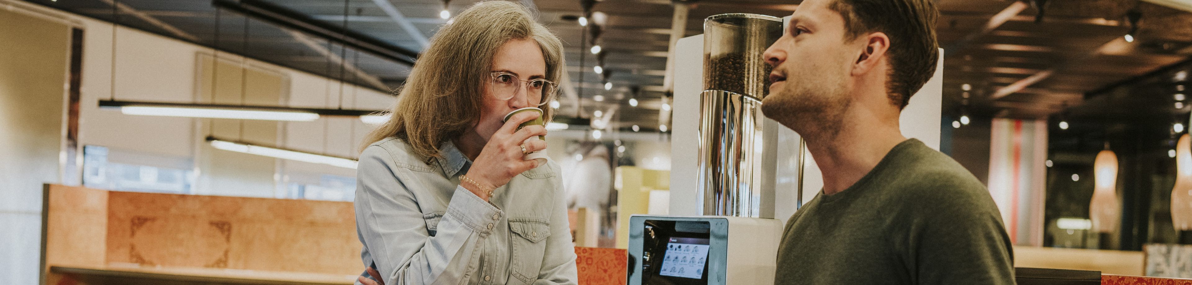 Een man en vrouw staan bij een koffieapparaat en drinken samen een kopje koffie.