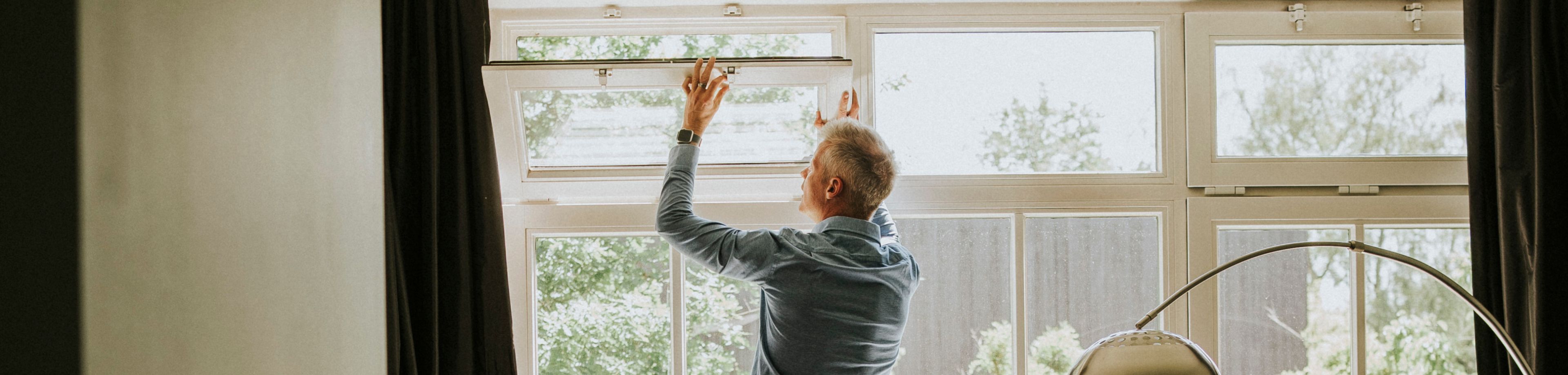 Man staat op kruk bij raampartij en opent kiepraam