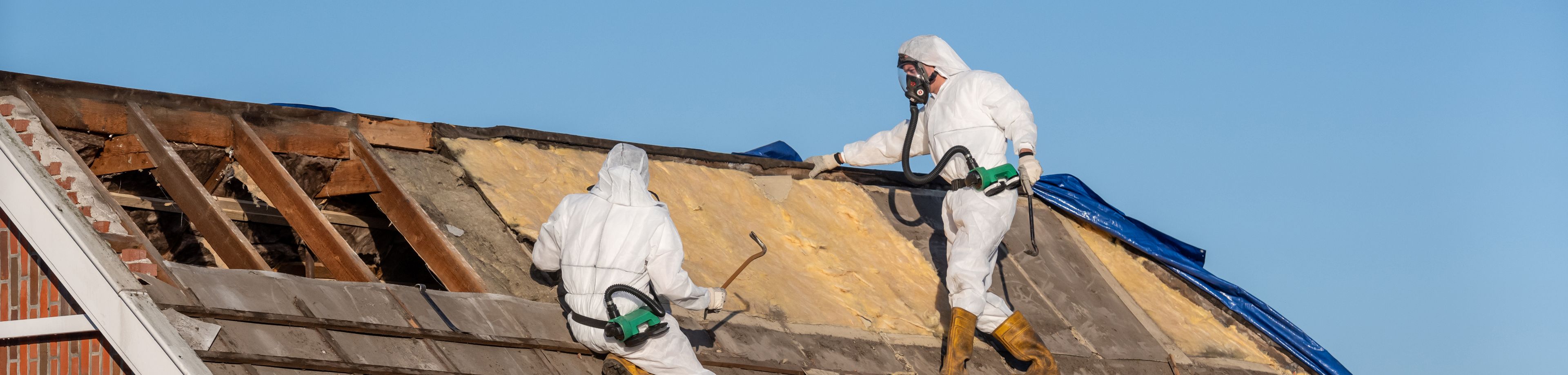 Mannen in witte pakken saneren een dak waarin asbest is verwerkt.