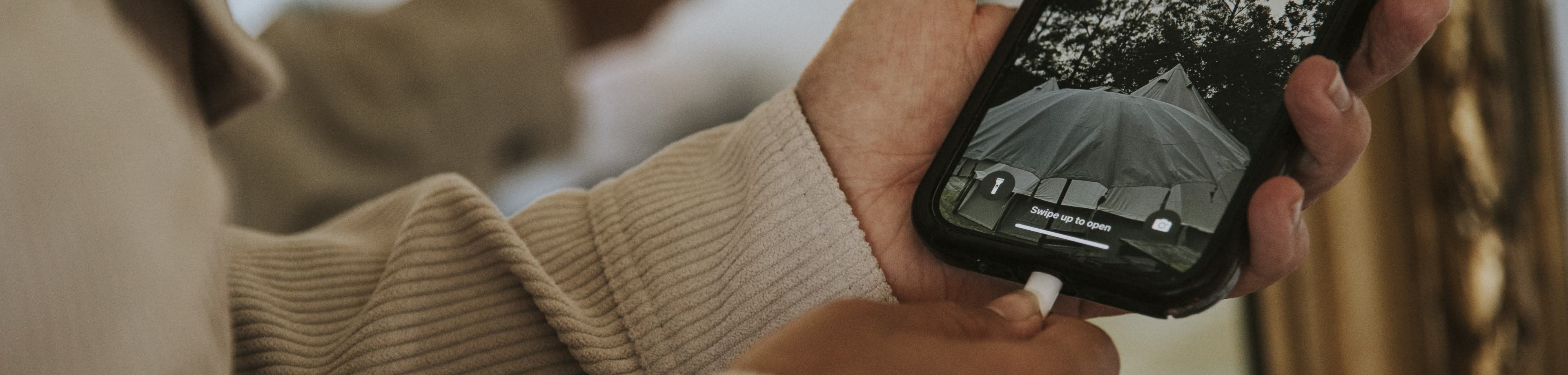 Een persoon houdt een mobiele telefoon in de hand, en steekt de oplaadkabel met de andere hand in de oplaadpoort van het toestel.