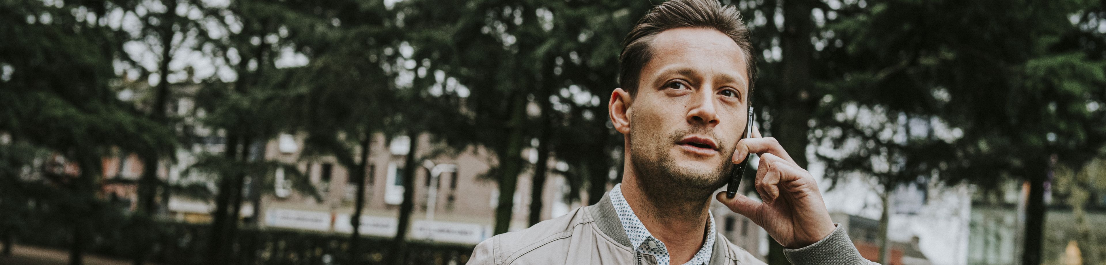 Een man staat in een tuin met een telefoon aan zijn oor.