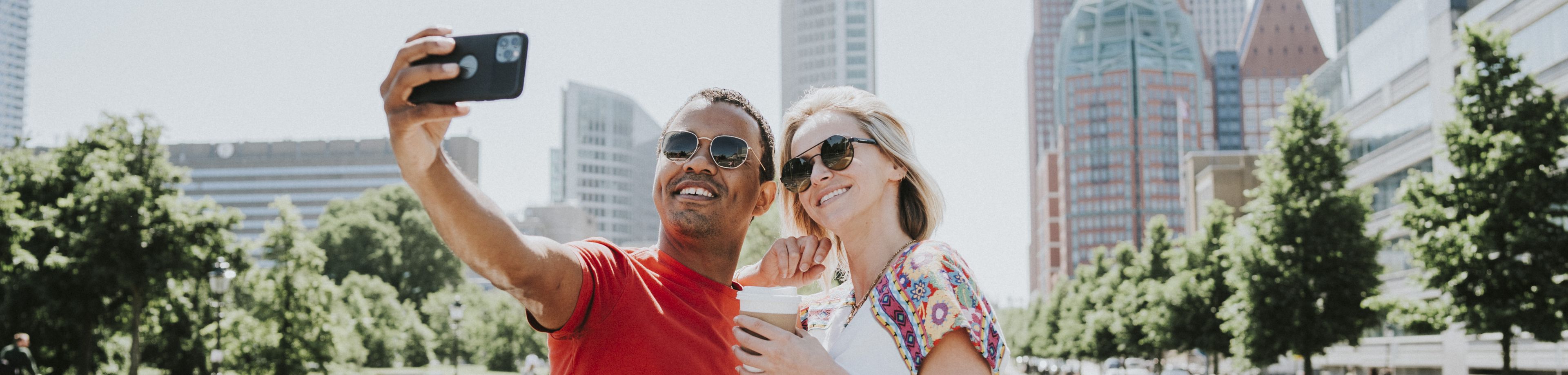 Man en vrouw staan op een brug, de man maakt een selfie, de vrouw heeft koffie in haar hand