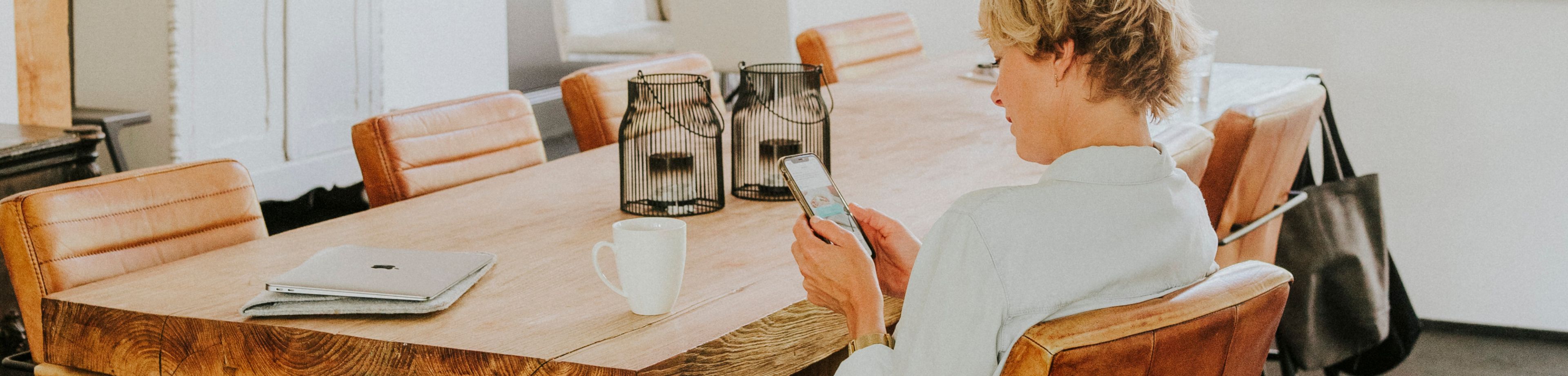 Vrouw zit aan tafel met de telefoon in de hand