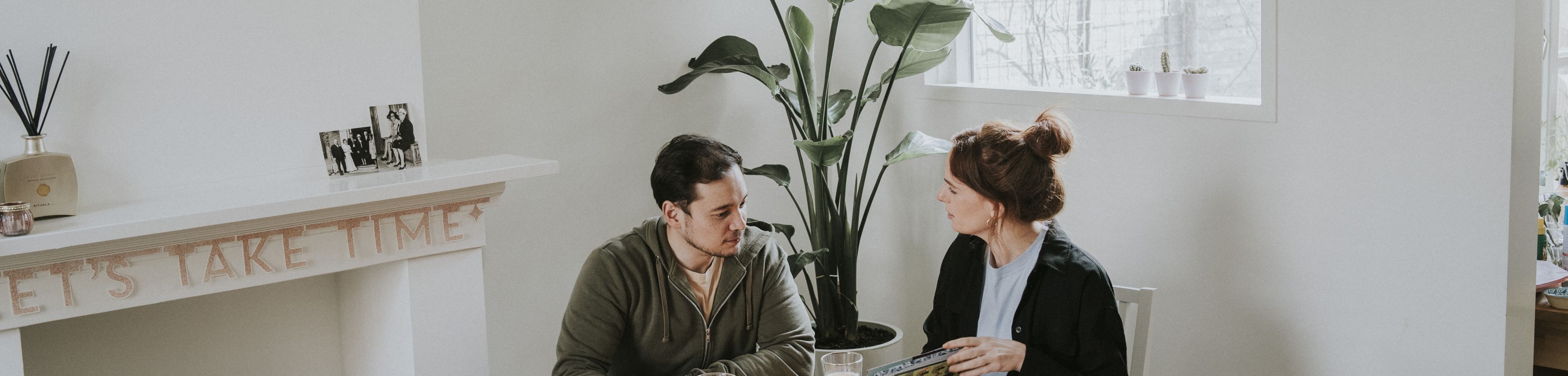 Man en vrouw zitten rond de keukentafel en zijn in gesprek met elkaar.