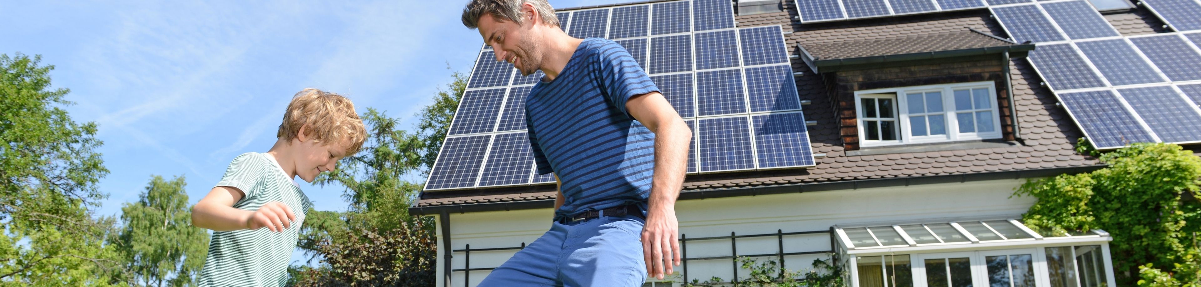 Een man voetbalt op een zonnige dag met zijn zoon in de tuin van het huis. Het dak van het huis ligt vol zonnepanelen.