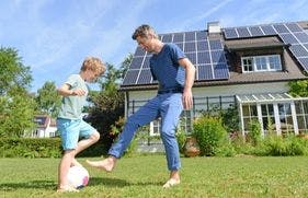 Een man voetbalt op een zonnige dag met zijn zoon in de tuin van het huis. Het dak van het huis ligt vol zonnepanelen.