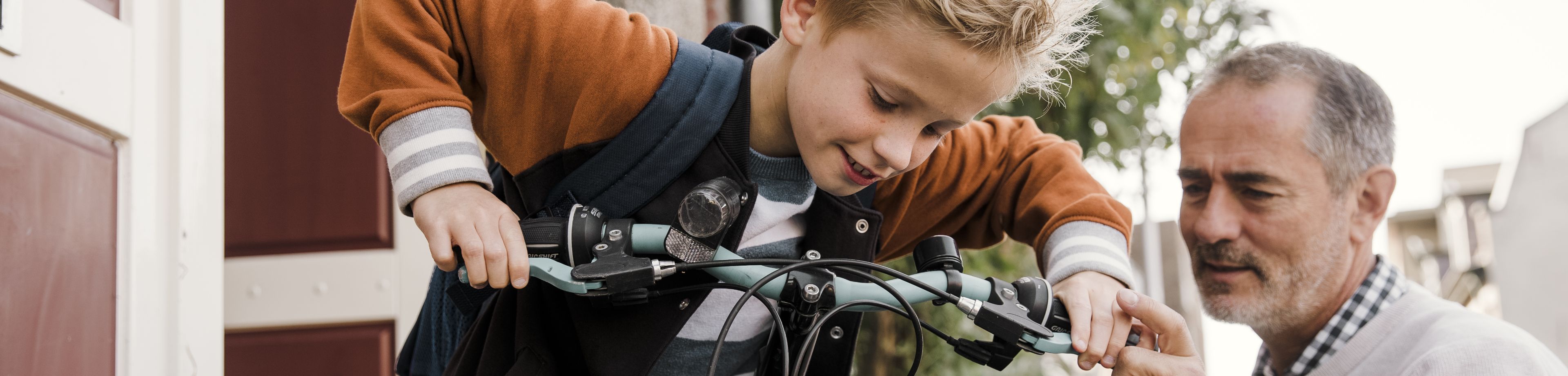Vader en zoon houden samen een kinderfiets vast.
