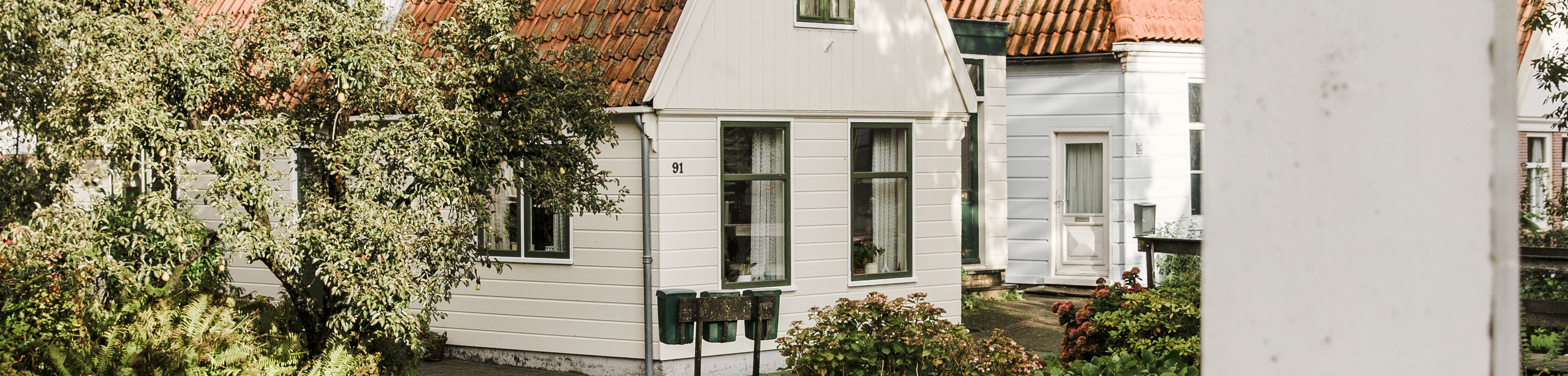 Een huis bekleed met wit hout en veel groen er omheen