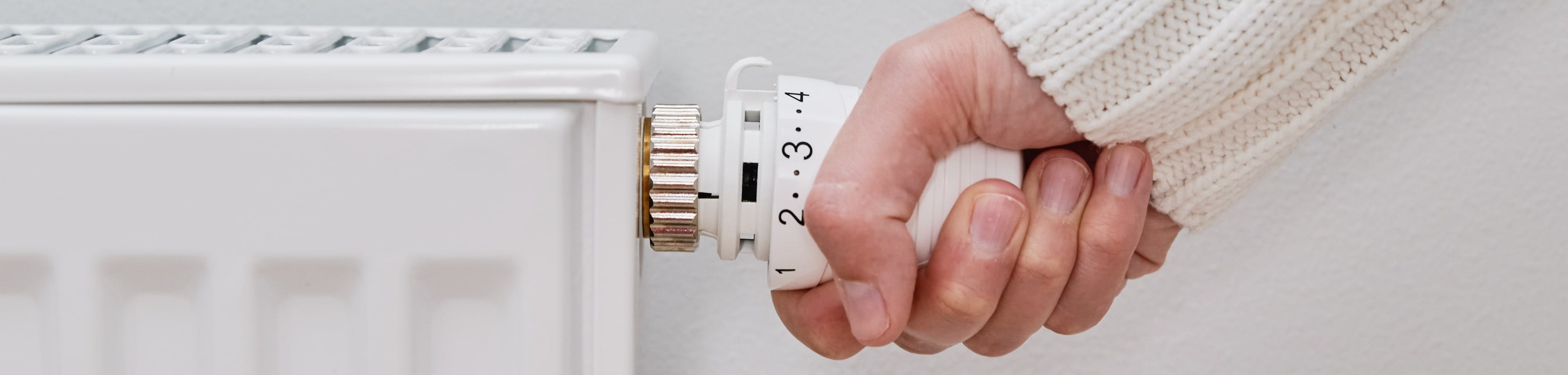Iemand pakt met 1 hand de thermostaatknop van de radiator vast, om de verwarming hoger of lager te kunnen zetten.
