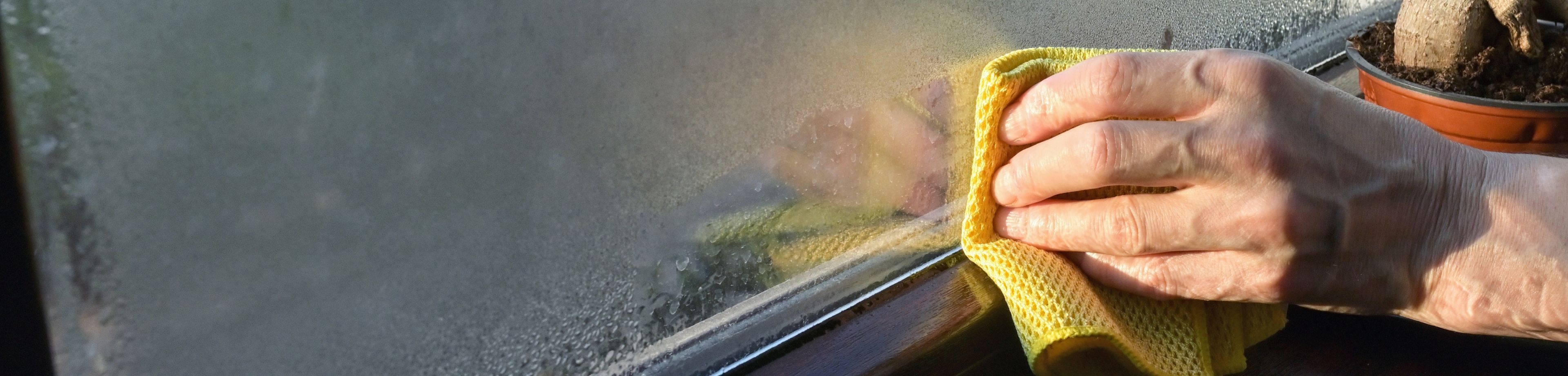 Iemand die het raam van een woning met een doekje afdoet