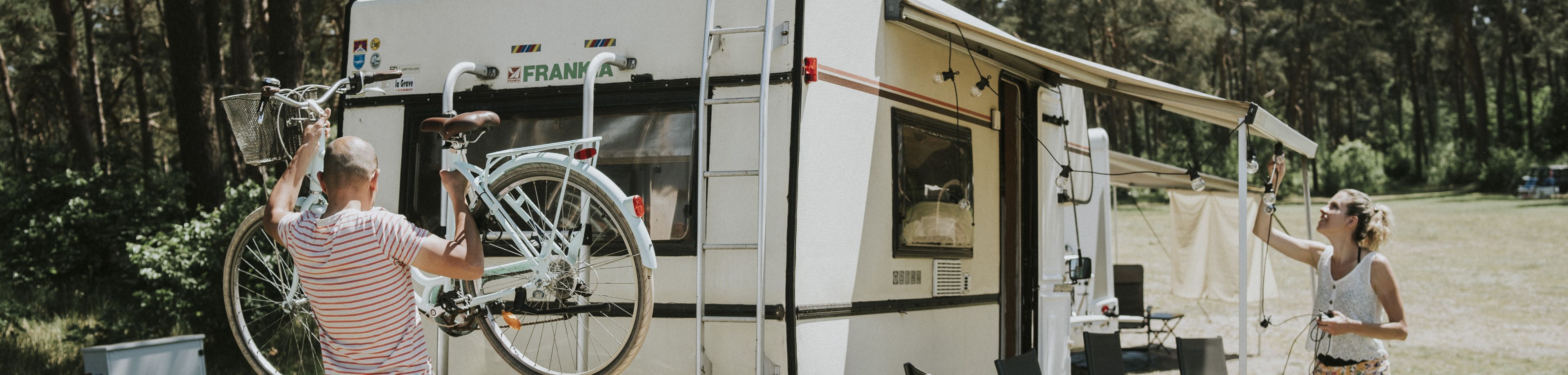 Stel is op reis met de camper. Vrouw hangt lampjes op en man haalt de fietsen van het rek.