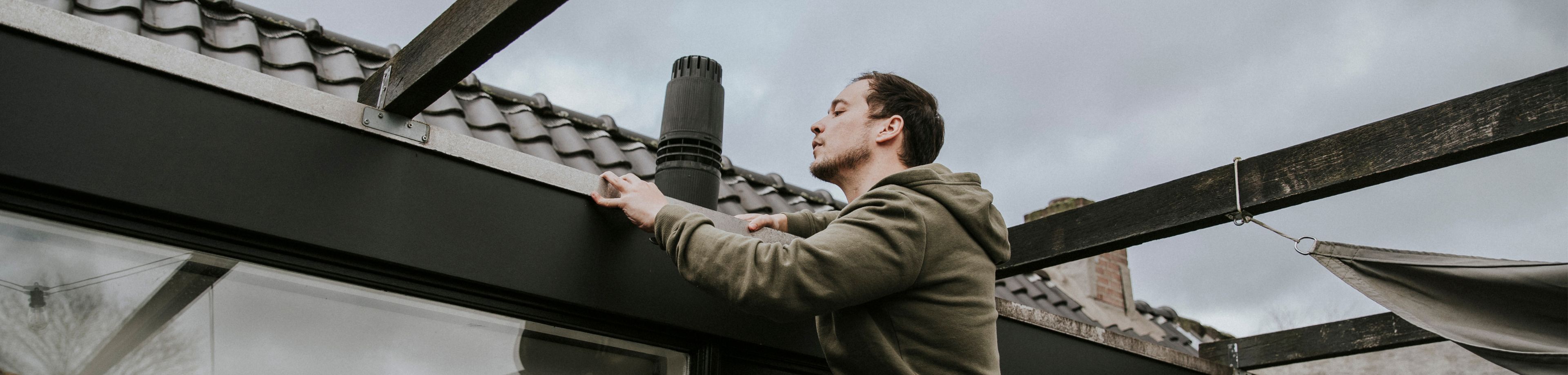 Een man inspecteert zijn dakgoot op mogelijke lekkages.