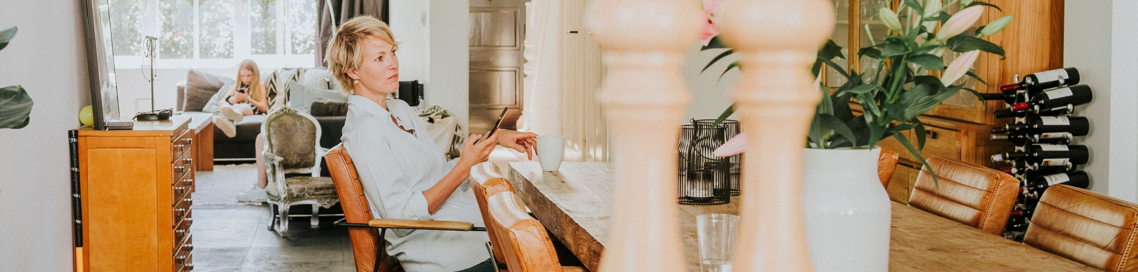 Vrouw zit aan de eettafel met een telefoon in haar hand