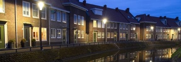Een rij huizen aan het water 's-avonds verlicht door straatlantaarns