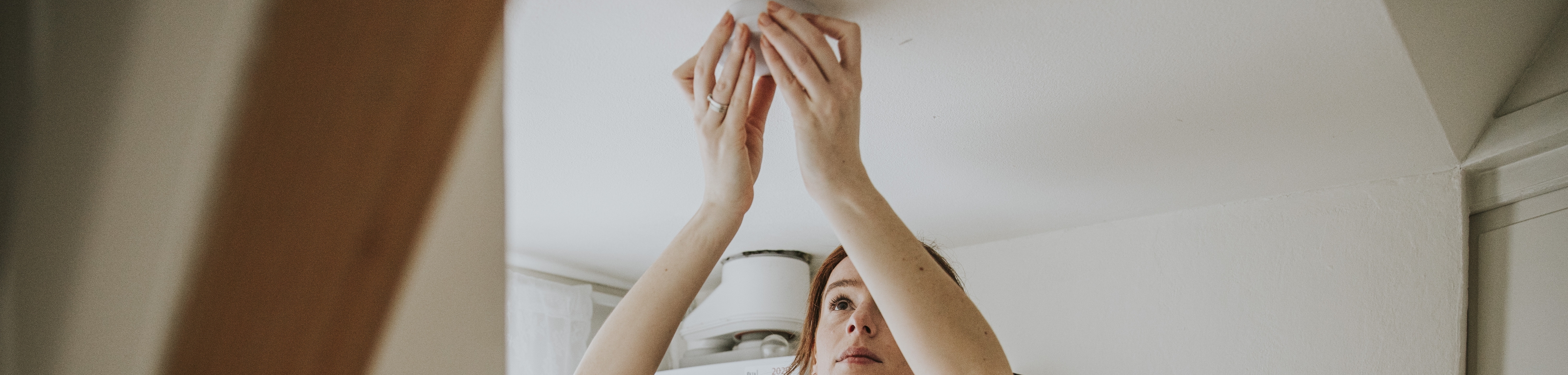 Een vrouw bevestigt een rookmelder aan het plafond