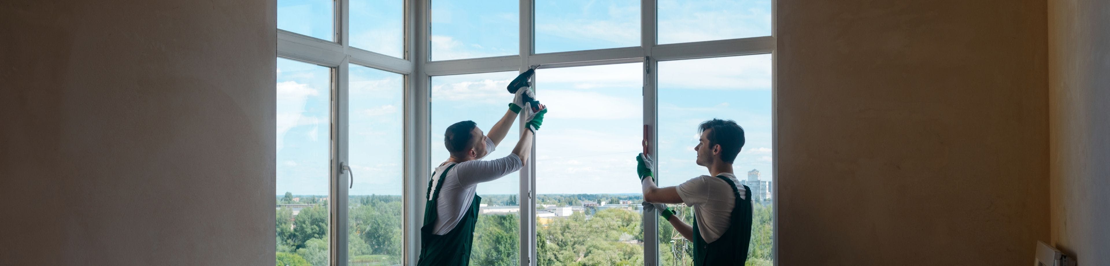 2 mannen in werk-overalls verrichten isolatiewerkzaamheden aan een raam.