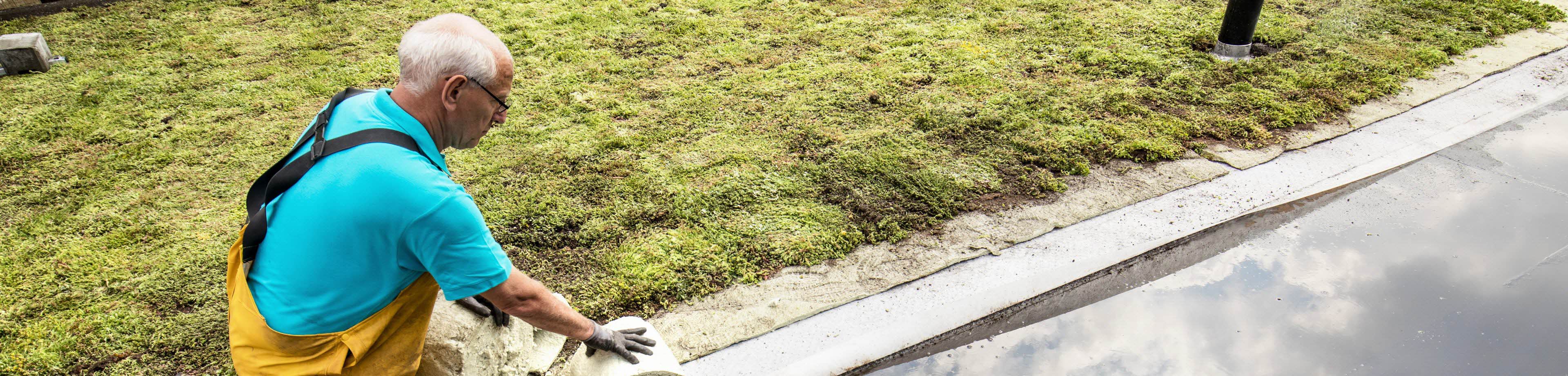 Een man zit op zijn knieën en is een dak aan het verduurzamen.