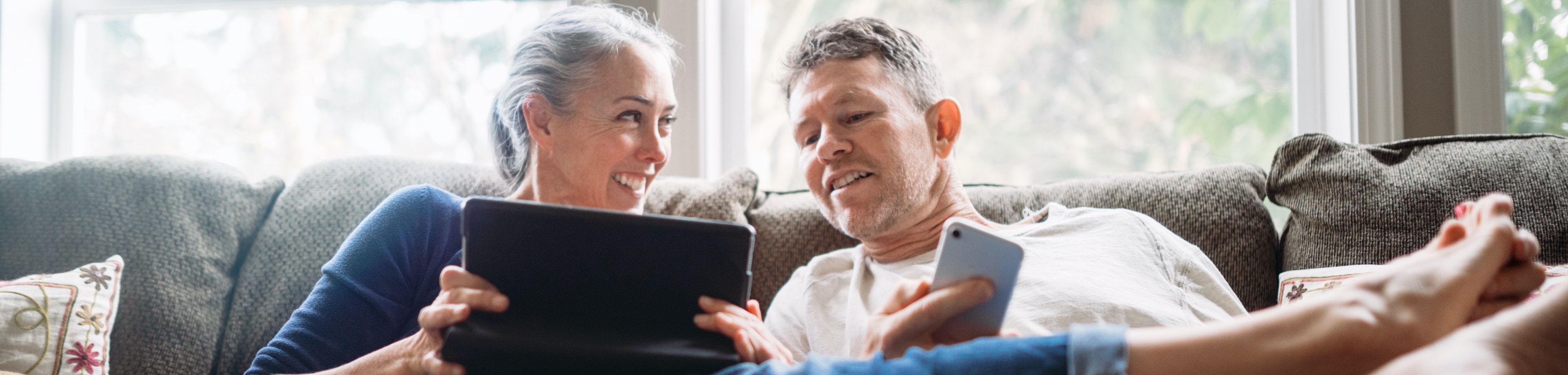 Man en vrouw die op de bank zitten en op hun tablet en smartphone bezig zijn