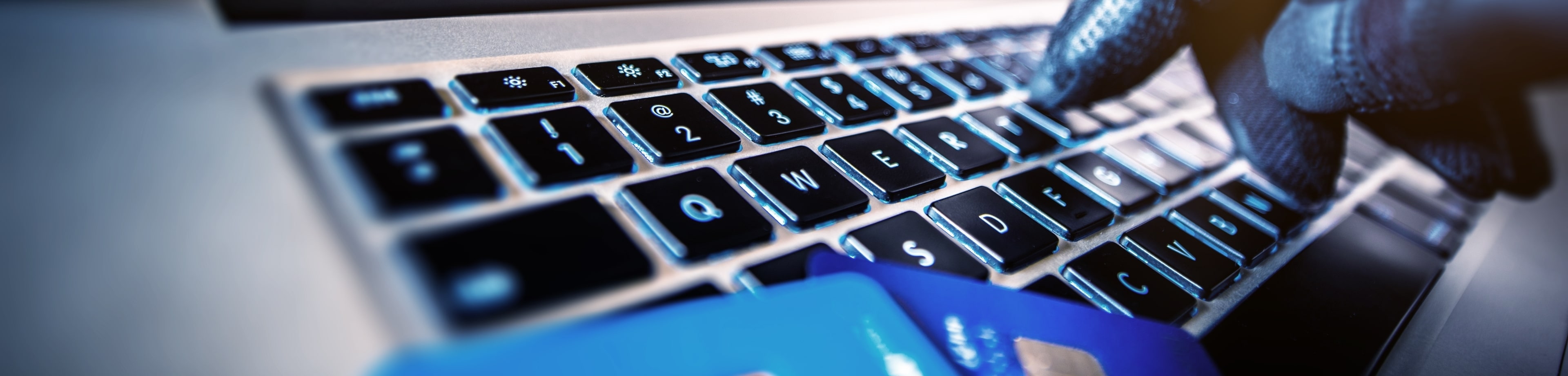 Een hand met een handschoen typt op een toetsenbord waar bankpasjes op liggen