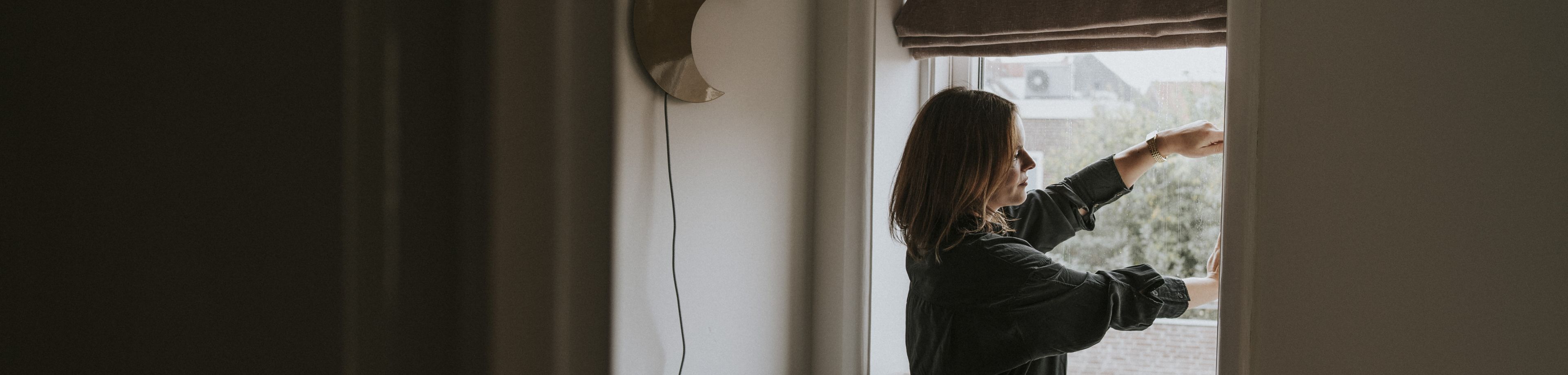 Een vrouw sluit het raam van de woonkamer om te voorkomen dat regen en wind naar binnen kunnen slaan.