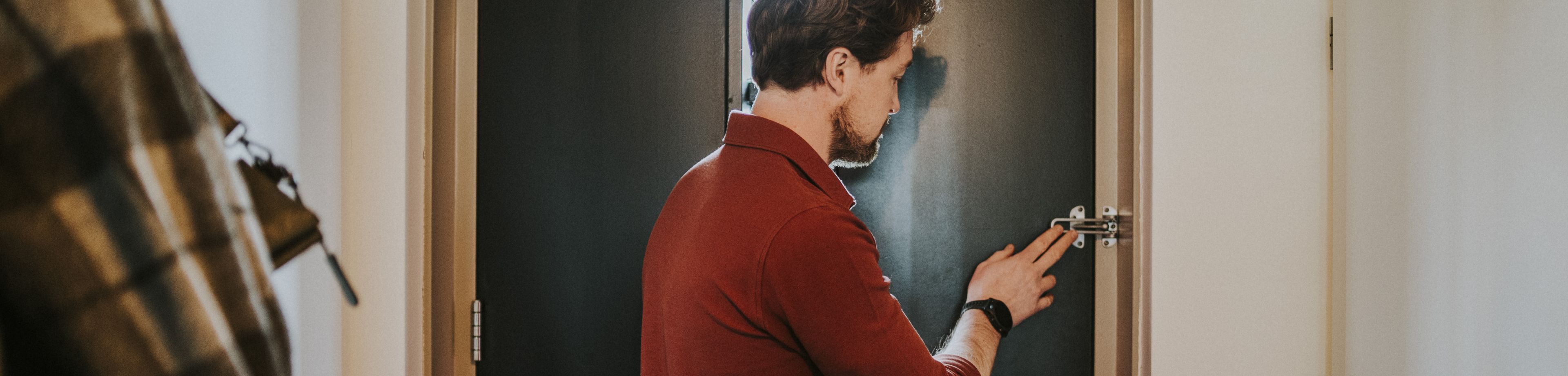 Een persoon sluit de extra deurgrendel van een voordeur, zodat deze extra beveiligd is tegen ongewenst bezoek.