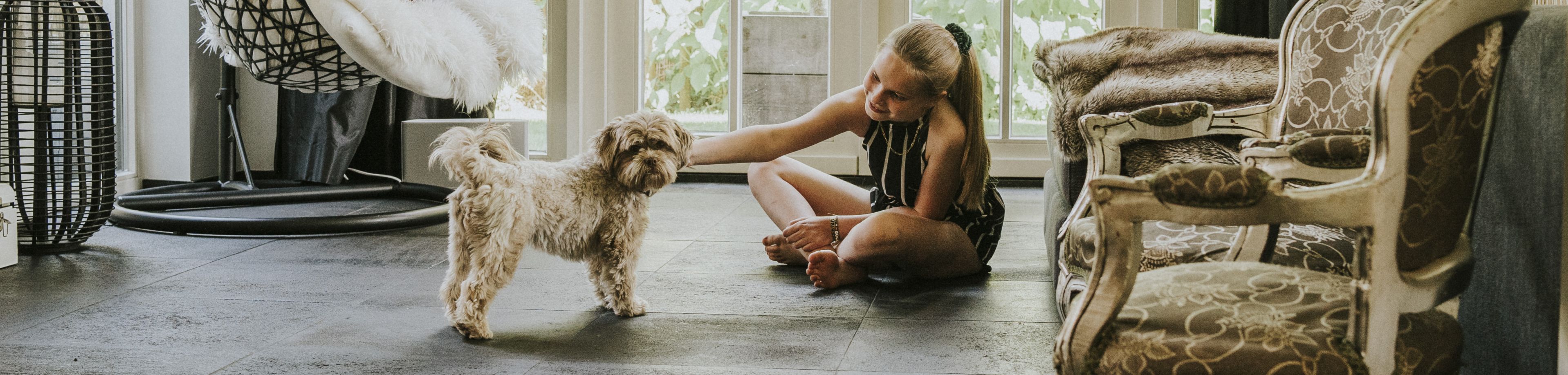 Een meisje zit in de woonkamer op de vloer en aait de hond.