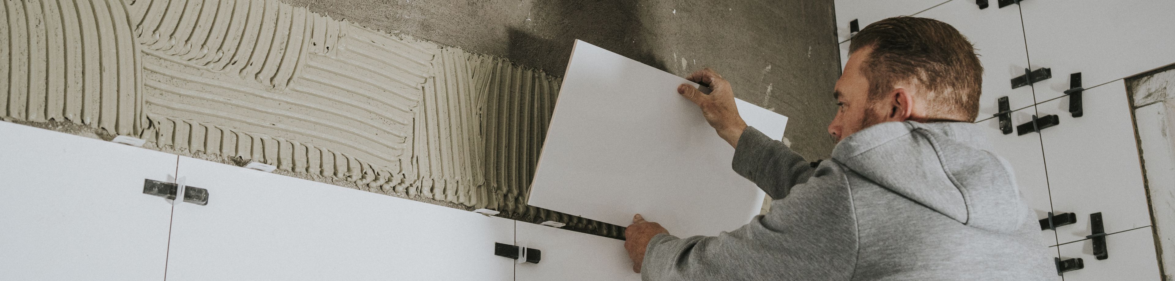 Een man plaatst witte wandtegels tegen de muur.