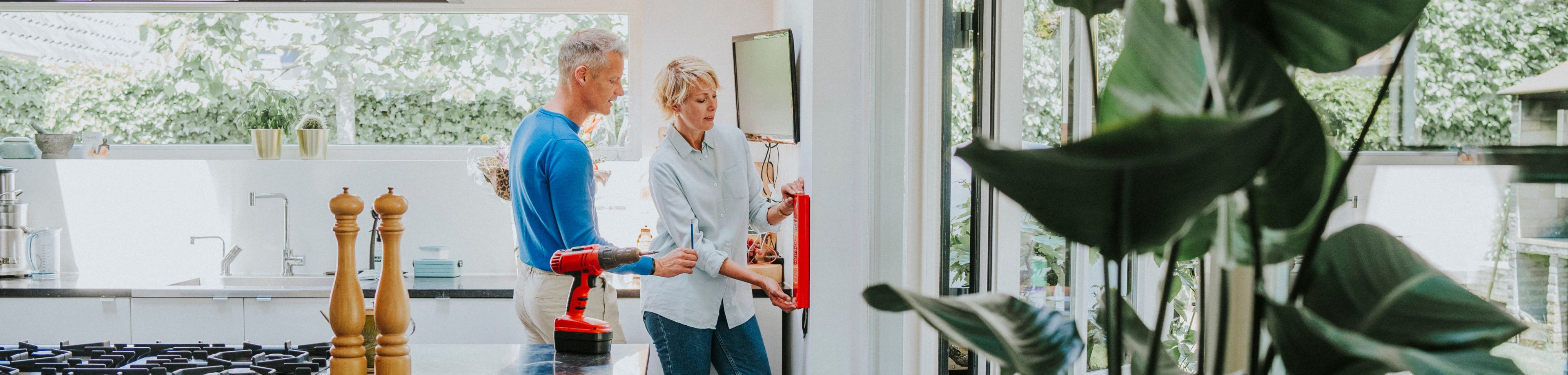 Een man en een vrouw bevestigen samen een blusdeken aan de muur in de keuken.