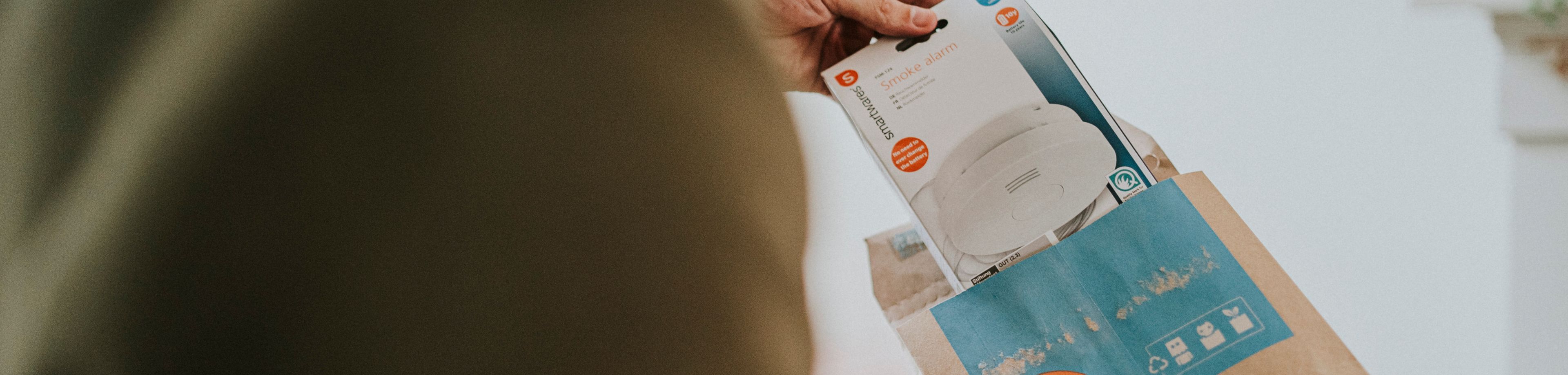 Iemand haalt een rookmelder uit de verpakking. Lees waar je op let als je een rookmelder koopt.