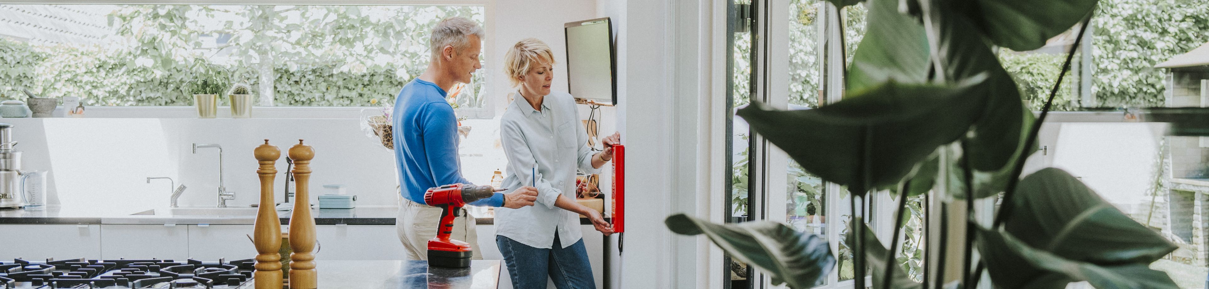 Een man en een vrouw staan in de keuken, en hangen samen een blusdeken aan de wand.