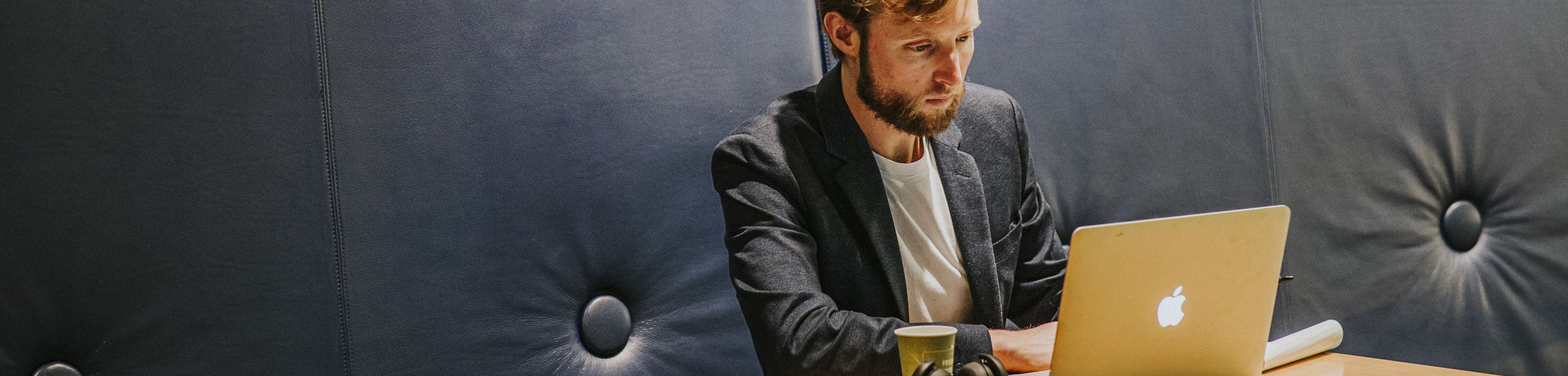 Een man werkt op zijn laptop, die op een tafeltje voor hem staat.