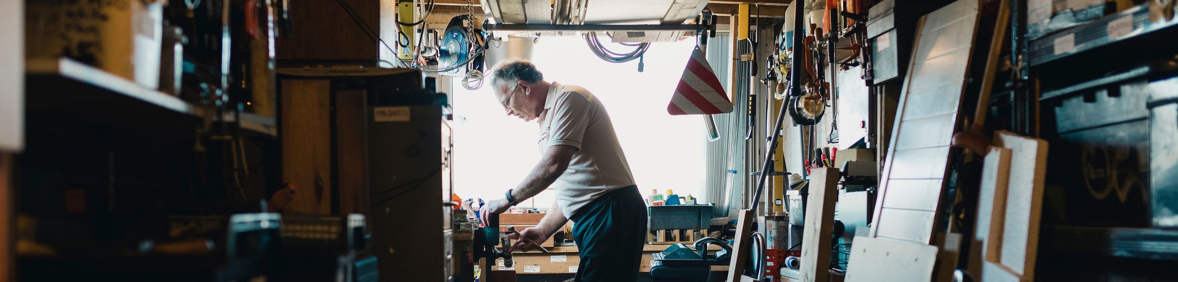 Oudere man staat in zijn schuur te werken aan de werkbank