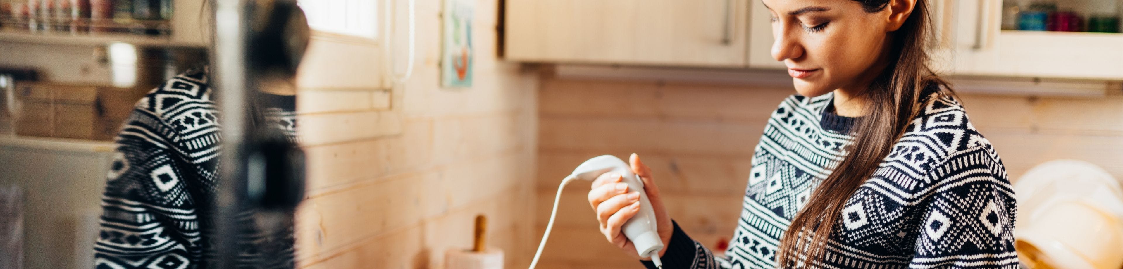 Vrouw in keuken met staafmixer. Lees hoe je de kans op kortsluiting en elektriciteitsschade in huis verkleint.