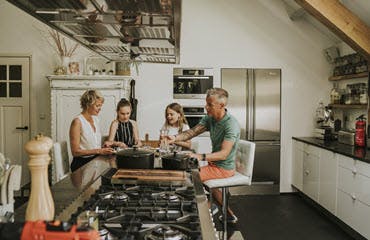 Een gezin met 2 dochters zit aan een kookeiland in een modern ingerichte keuken te eten.