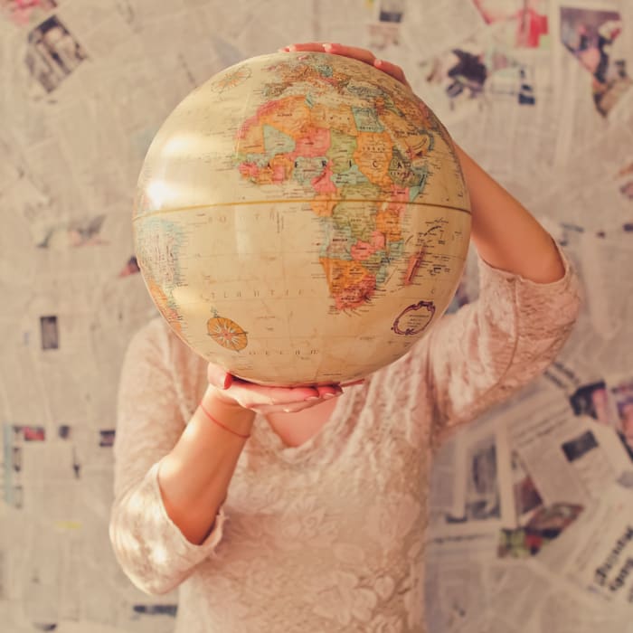 Vrouw houdt wereldbol vast voor haar hoofd.