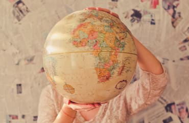 Vrouw houdt wereldbol vast voor haar hoofd.