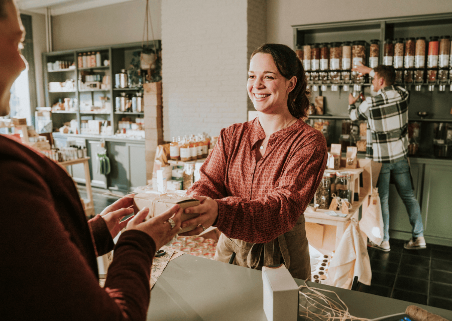 Een jonge vrouw geeft met een lach op haar gezicht een mooi ingepakt doosje aan een andere vrouw