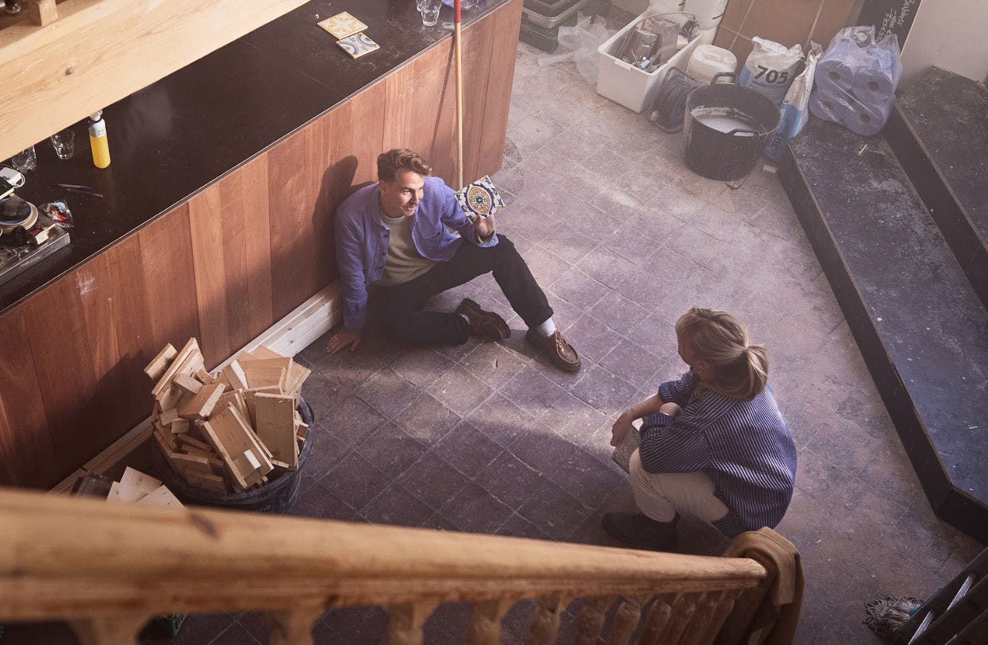 Een man en vrouw zijn samen tegels aan het uitzoeken voor hun bedrijfspand. Ze zitten samen op de grond. De foto is van bovenaf genomen.