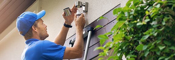 Man die een buitenlamp met sensor bij een woning installeert. Dit verkleint de kans op een woninginbraak.